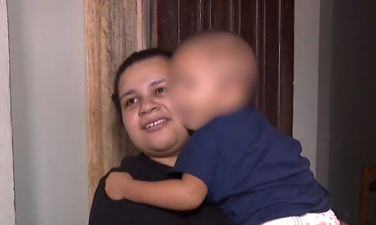 Mãe segura no colo a filha de 3 anos que recebeu alta após ser baleada na cabeça em atentado na Grande Curitiba.