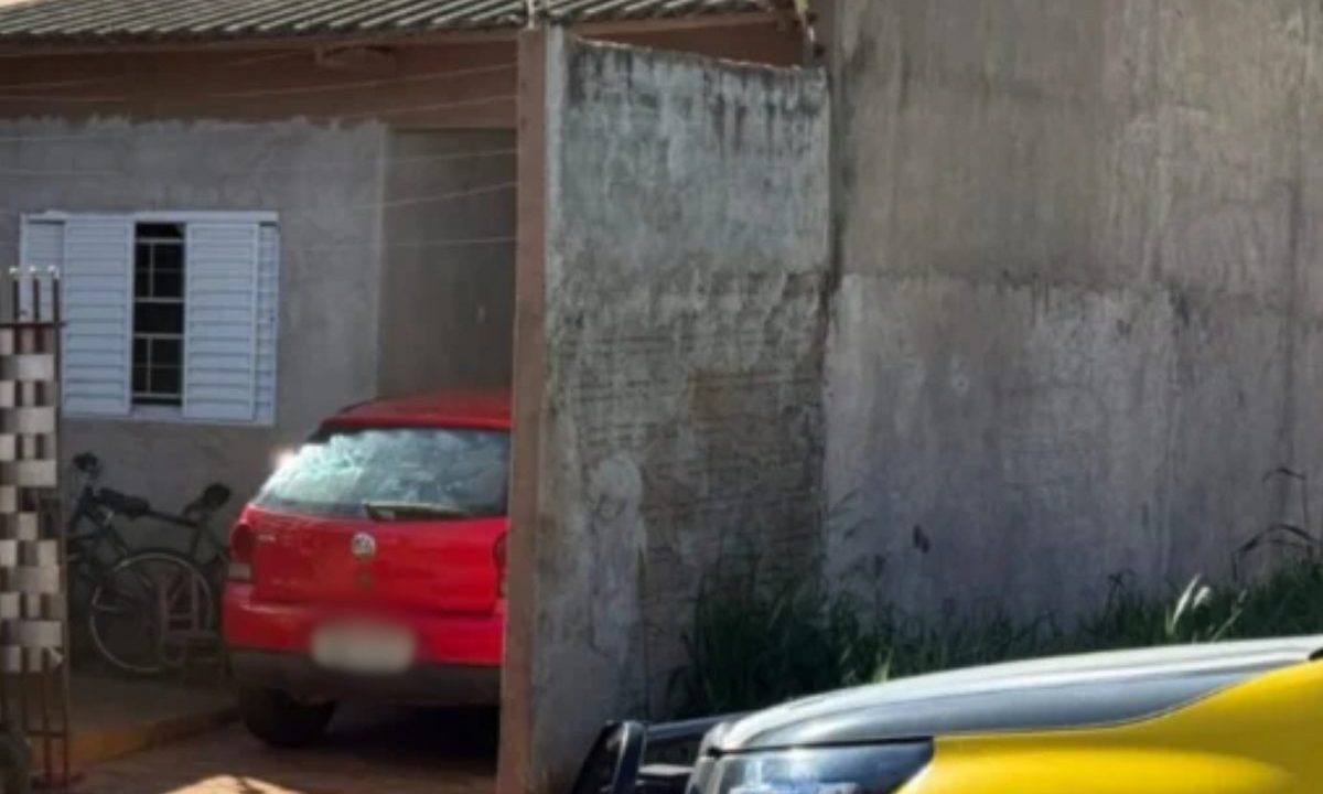 Menina de 9 anos é baleada enquanto dormia ao lado da avó. Imagem mostra cena do crime. Um carro vermelho está na garagem. Viatura da Polícia Militar do lado de fora.