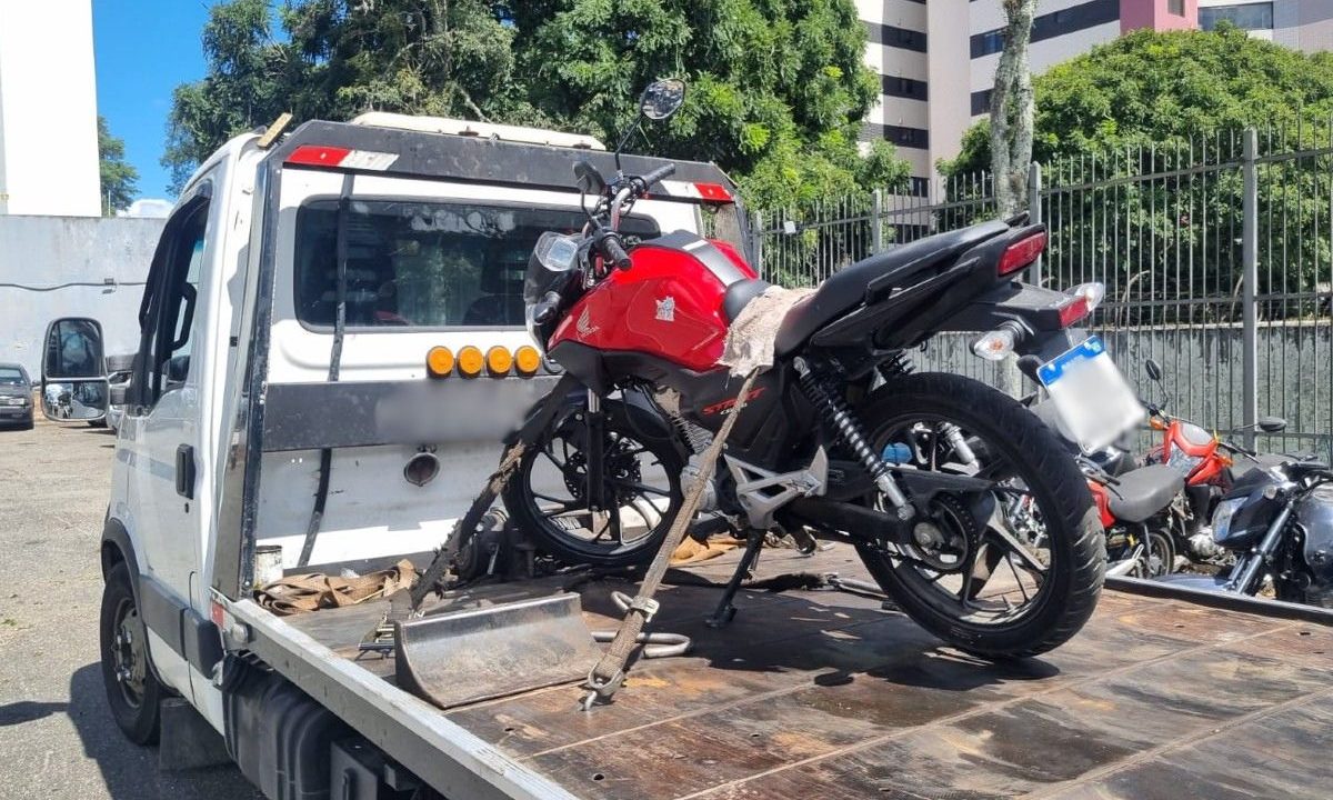 Moto vermelha posicionada sobre um guincho, dentro do pátio de uma delegacia, após ter sido furtada e posteriormente recuperada pela polícia em Curitiba.