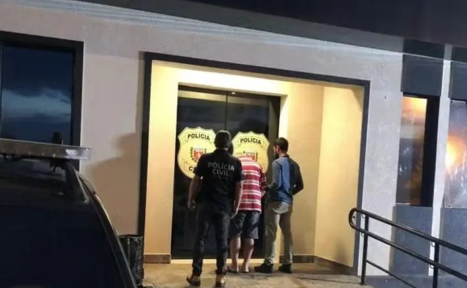 Foto mostra motorista de transporte escolar preso por abuso sexual de crianças algemado em frente a uma delegacia