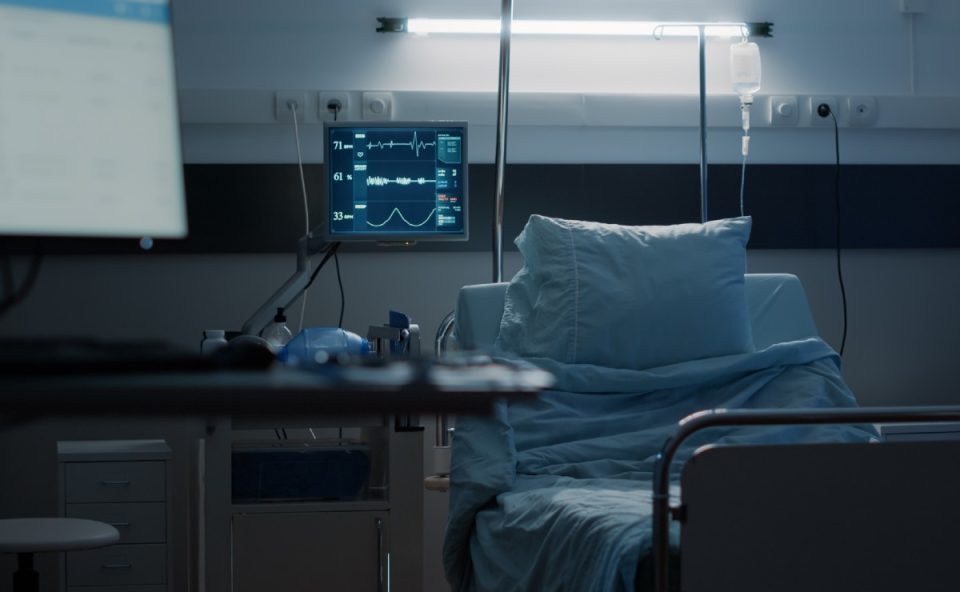 Leito hospitalar vazio em quarto com equipamentos médicos e monitor ligado, ilustrando a situação de retorno de funcionários em hospital de Curitiba após demissões sem pagamentos.