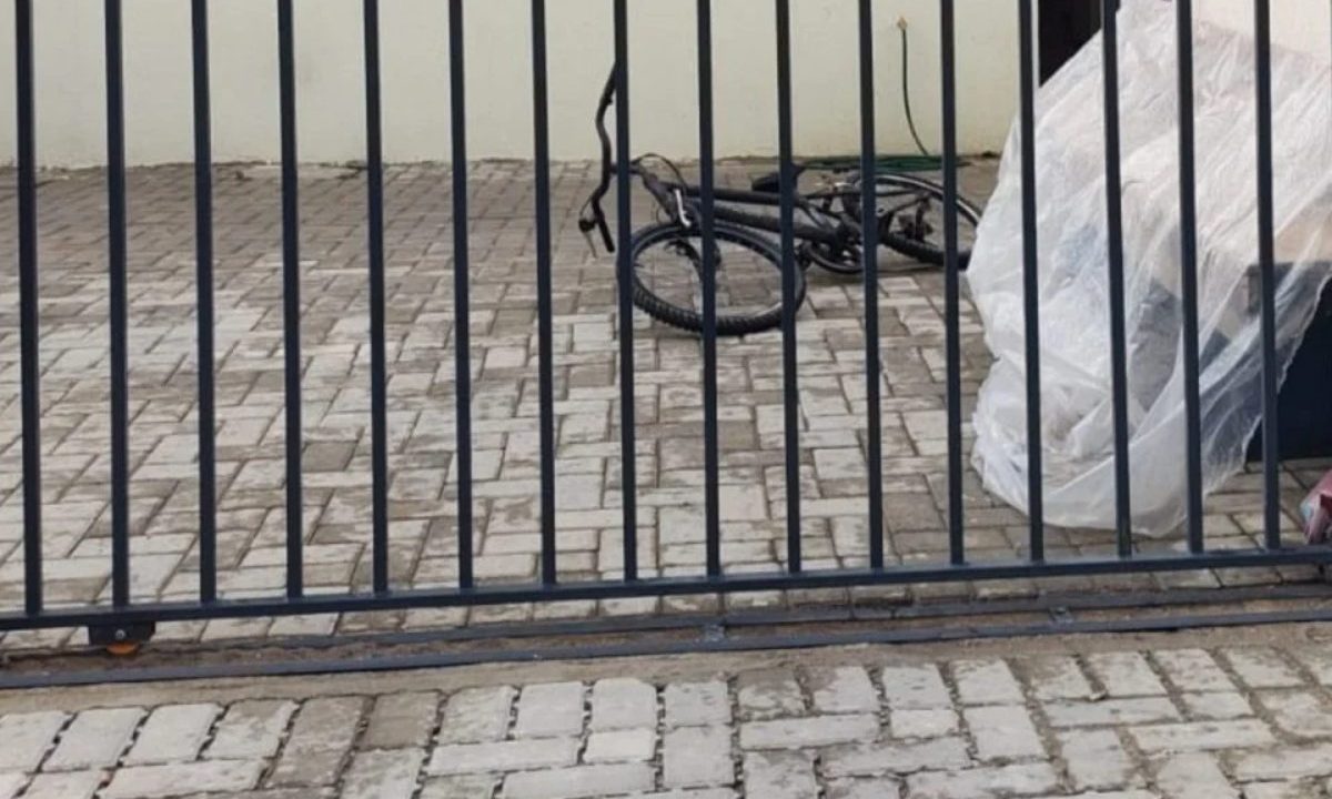 Mulher que sofreu tentativa de feminicídio no Dia Internacional da Mulher tinha medida protetiva e vive escondida. Imagem mostra um portão e uma bicicleta caída.