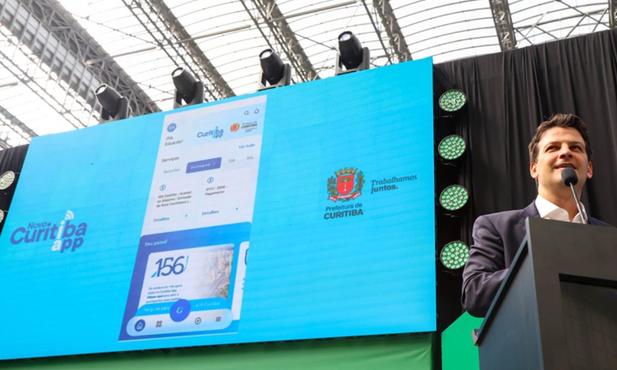 Prefeito de Curitiba apresenta o novo Curitiba App em telão durante evento, com interface do aplicativo exibida ao público.
