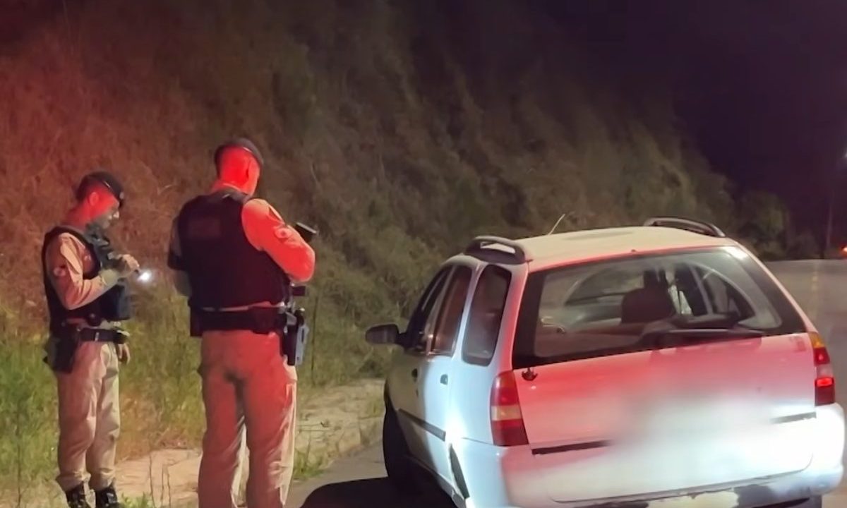 Pai é assaltado por dois suspeitos ao buscar filha na faculdade no Centro de Curitiba. Imagem mostra dois policiais ao lado de um veículo branco, que foi levado por criminosos.