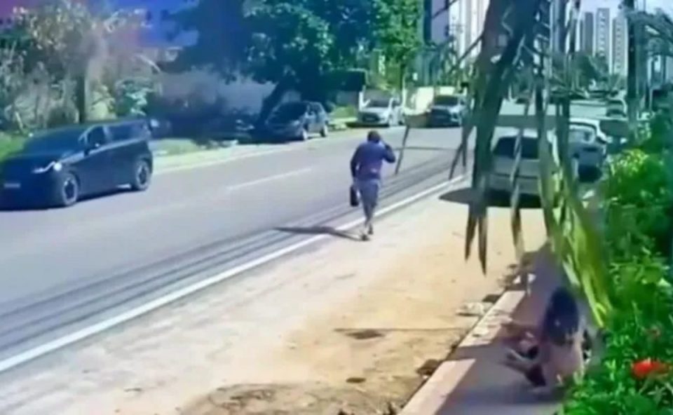 Imagem mostra o paranaense assassinado a tiros no Nordeste caminhando na rua. Ele aparece de costas. A rua está vazia, apenas com carros estacionados. Há duas meninas ao lado conversando.