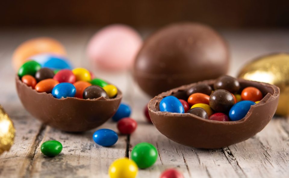 Metades de ovos de Páscoa de chocolate recheadas com confeitos coloridos sobre mesa de madeira