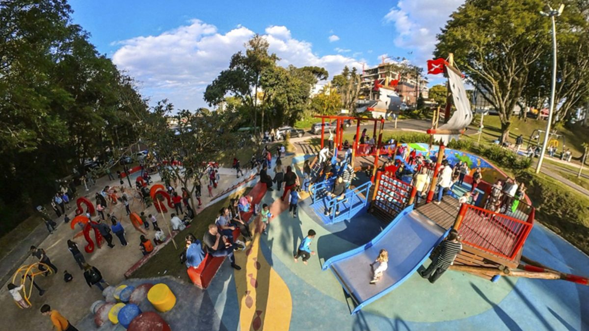 Parque infantil com temática de pirata Zulmiro, com brinquedos coloridos, escorregador e famílias com crianças aproveitando o espaço ao ar livre.