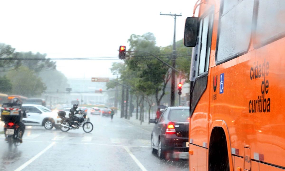 Imagem mostra a previsão do tempo em Curitiba. Foto aparece um ônibus laranja de Curitiba em um dia chuvoso na rua.
