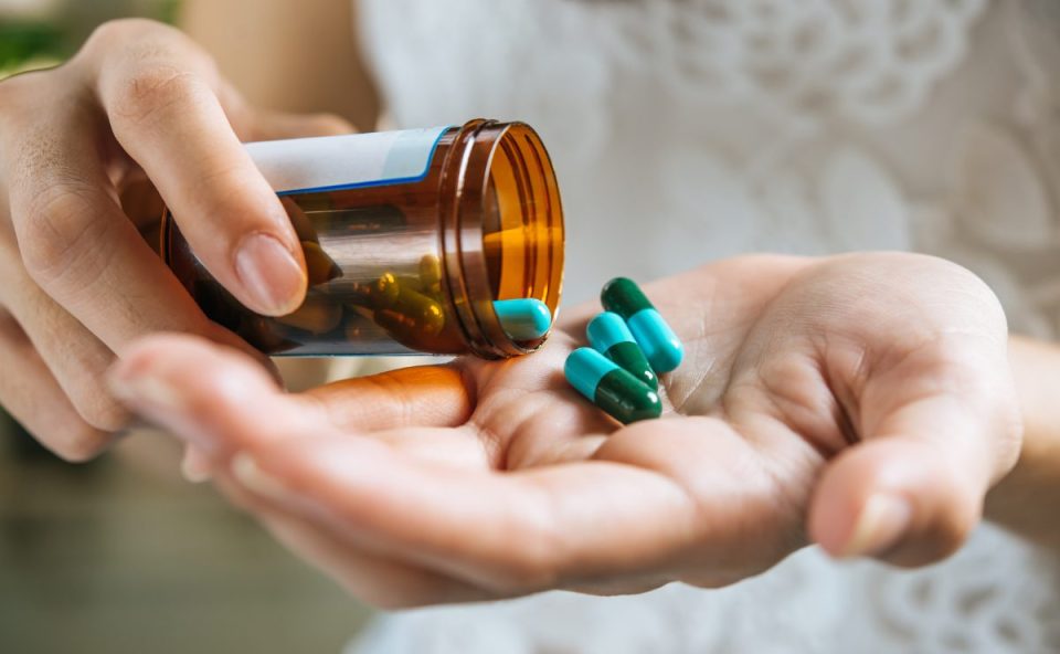 pessoa segurando cápsulas na mão enquanto despeja medicamentos de um frasco que terão reajuste em abril