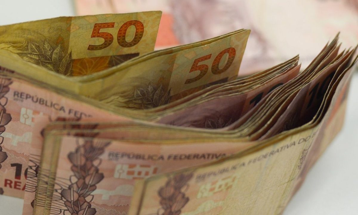Foto de cédulas de reais em pé, em cima de uma mesa; dinheiro usado para ilustrar o valor que será recebido pelo paranaense com o resultado da loteria federal 6052