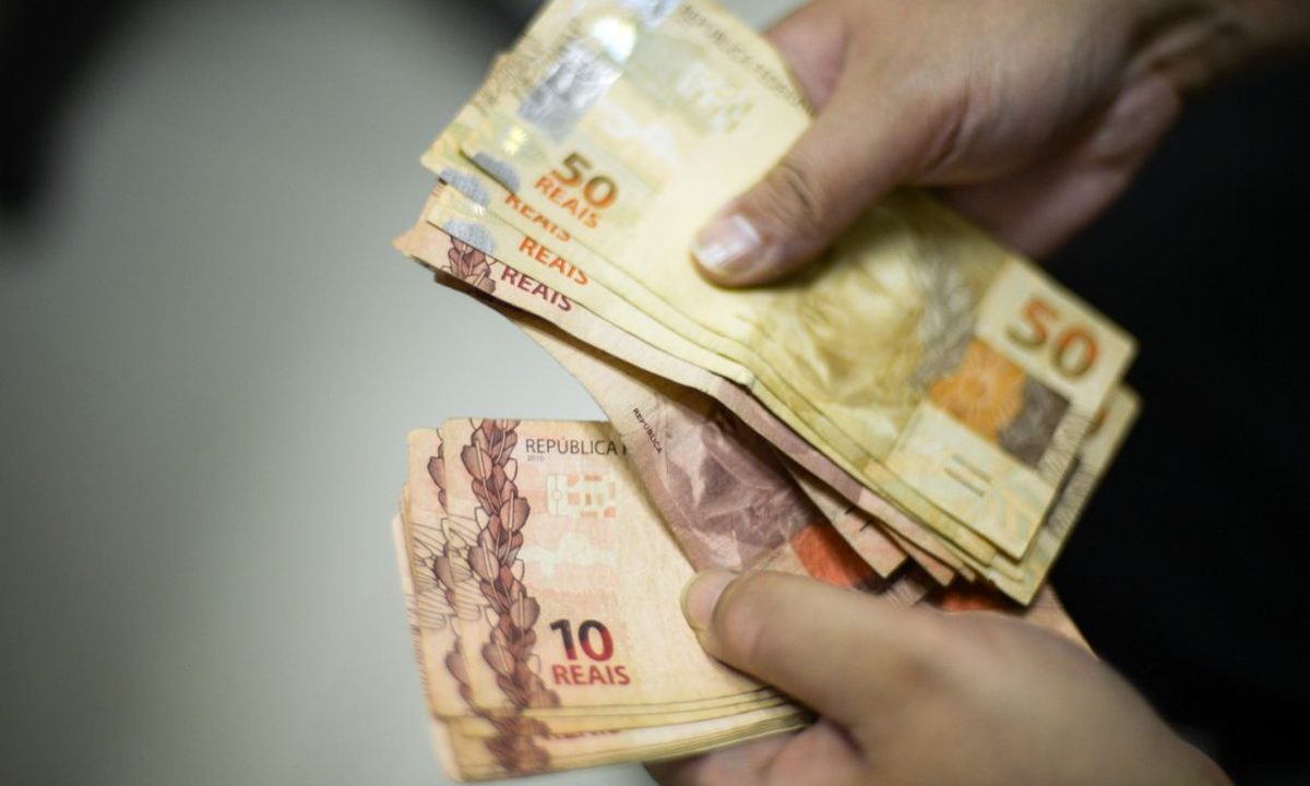 A foto mostra uma pessoa manuseando cédulas de 10 e 50 reais