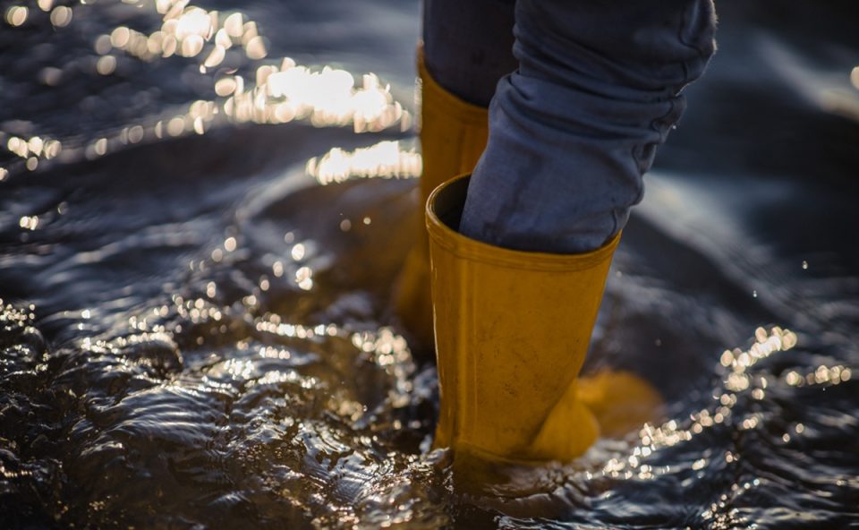 Pessoa andando em área de enchente usando bota de proteção. Sesa alerta para o risco da leptospirose com aumento de chuvas