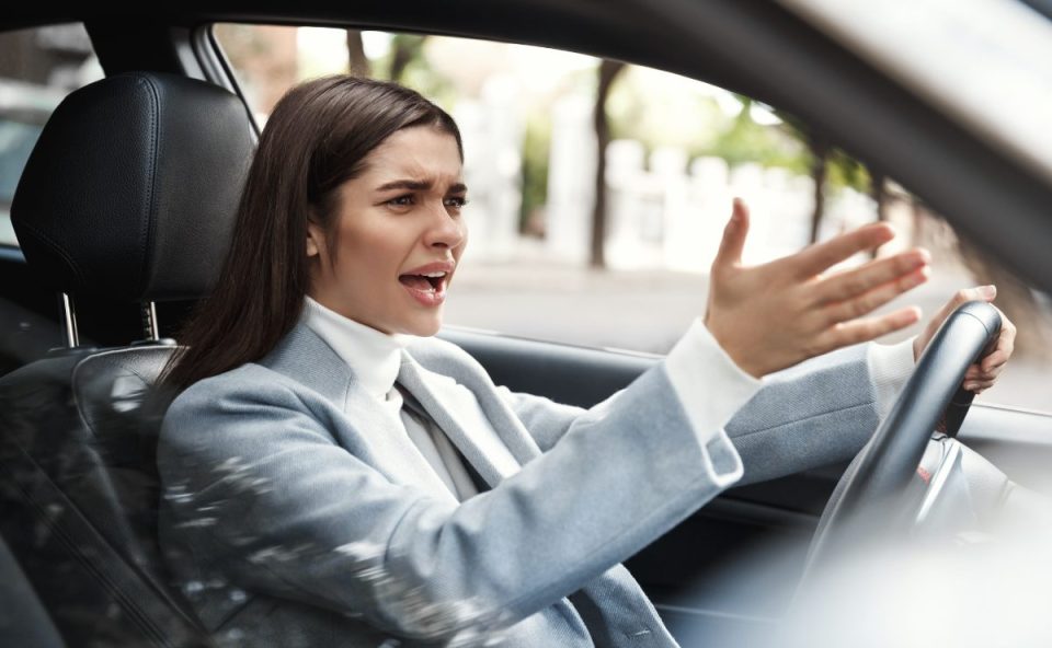 Motorista irritada gesticula dentro do carro durante discussão no trânsito, ilustrando situação de violência no trânsito