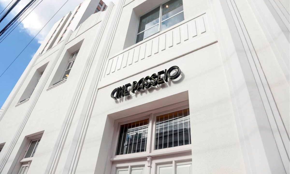 Fachada branca de arquitetura clássica do Cine Passeio em Curitiba, vista de baixo para cima, com o letreiro preto em destaque contra o céu.