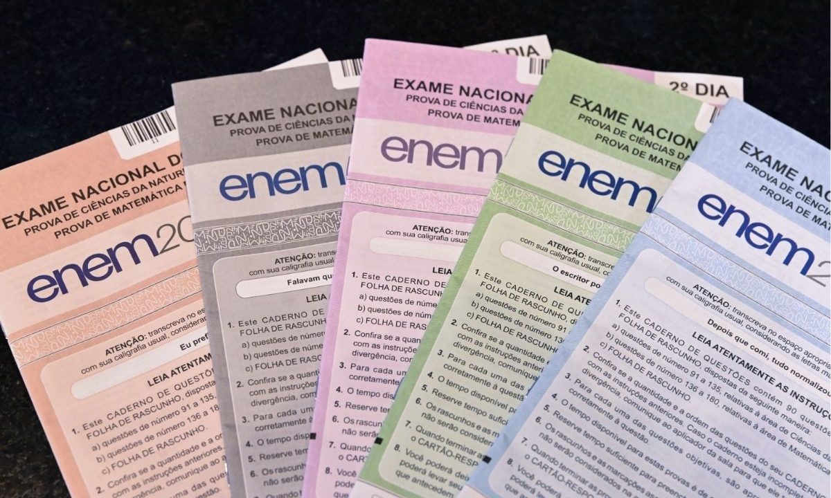 Cinco cadernos de prova do Enem em cores diferentes (rosa, cinza, roxo, verde e azul) organizados lado a lado. No topo de cada caderno, lê-se "Exame Nacional do Ensino Médio" e o logotipo do Enem. Imagem ilustrativa para matéria referente ao prazo para pedir isenção e justificar ausência no Enem 2026, que encerra na próxima semana.