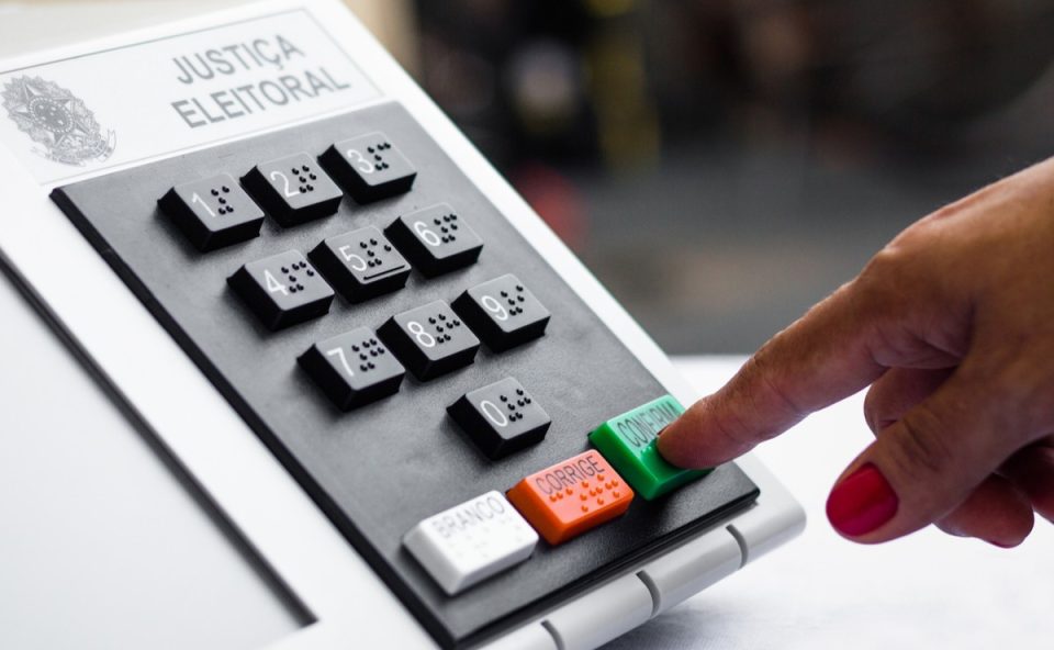 Dedo com unha pintada apertando o botão confirma na Urna, momento necessário para votar nos candidatos governadores que vão disputar as eleições 2026