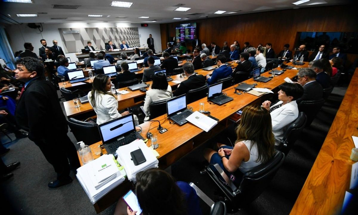 Vista geral da sala da Comissão de Constituição e Justiça (CCJ) do Senado Federal em Brasília, com senadores sentados às mesas com notebooks durante sessão.