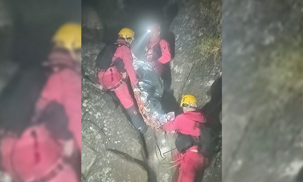 A imagem mostra os bombeiros segurando uma maca onde está uma mulher no meio das pedras da trilha