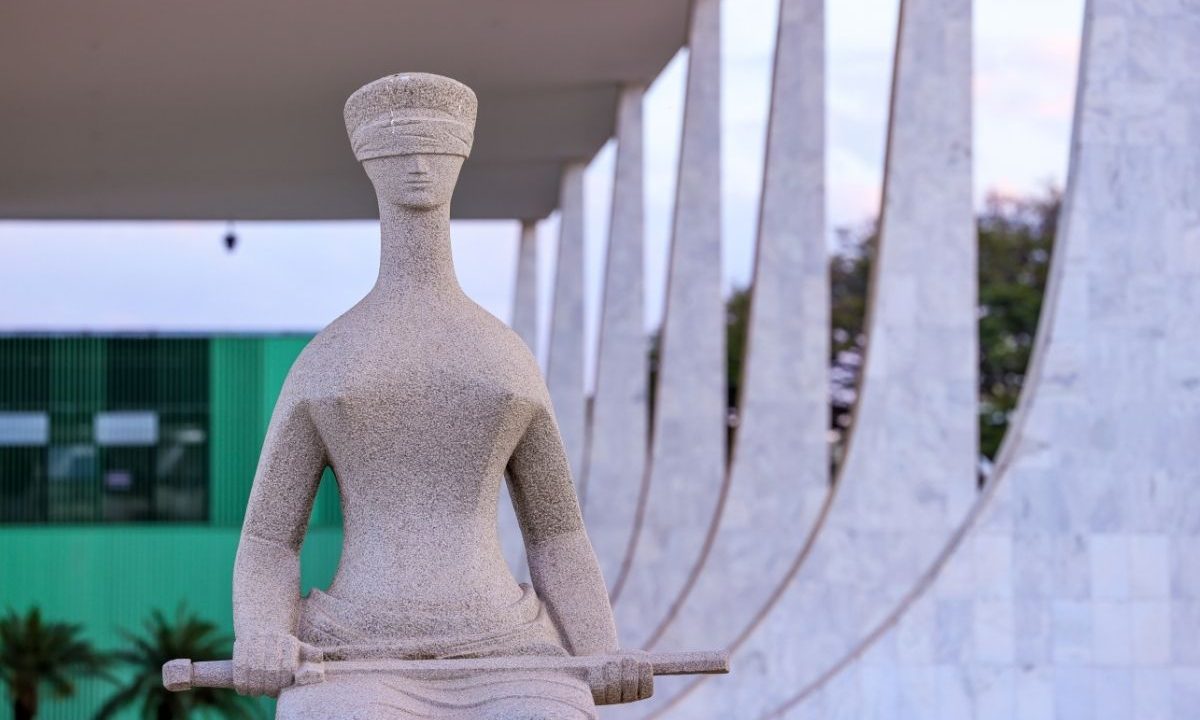 Close frontal da estátua "A Justiça", de Alfredo Ceschiatti, localizada em frente ao prédio do Supremo Tribunal Federal (STF) em Brasília. Ao fundo, as colunas do Palácio do STF sob luz suave