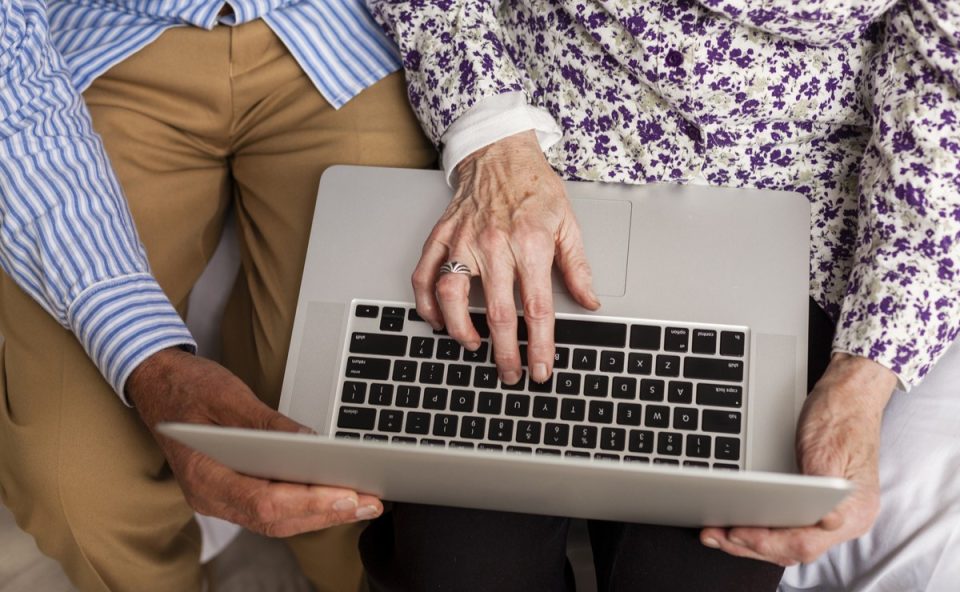 Mãos de idosos mexendo no computador visto de cima, ilustrando momento da declaração de imposto de renda