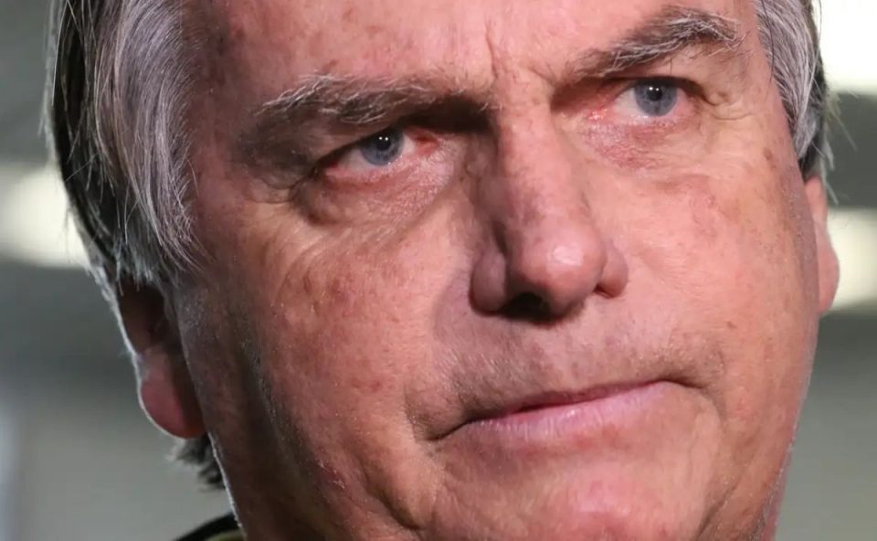 Close do rosto do ex-presidente Jair Bolsonaro, com expressão séria, olhando para o lado. A iluminação destaca os detalhes de seu rosto