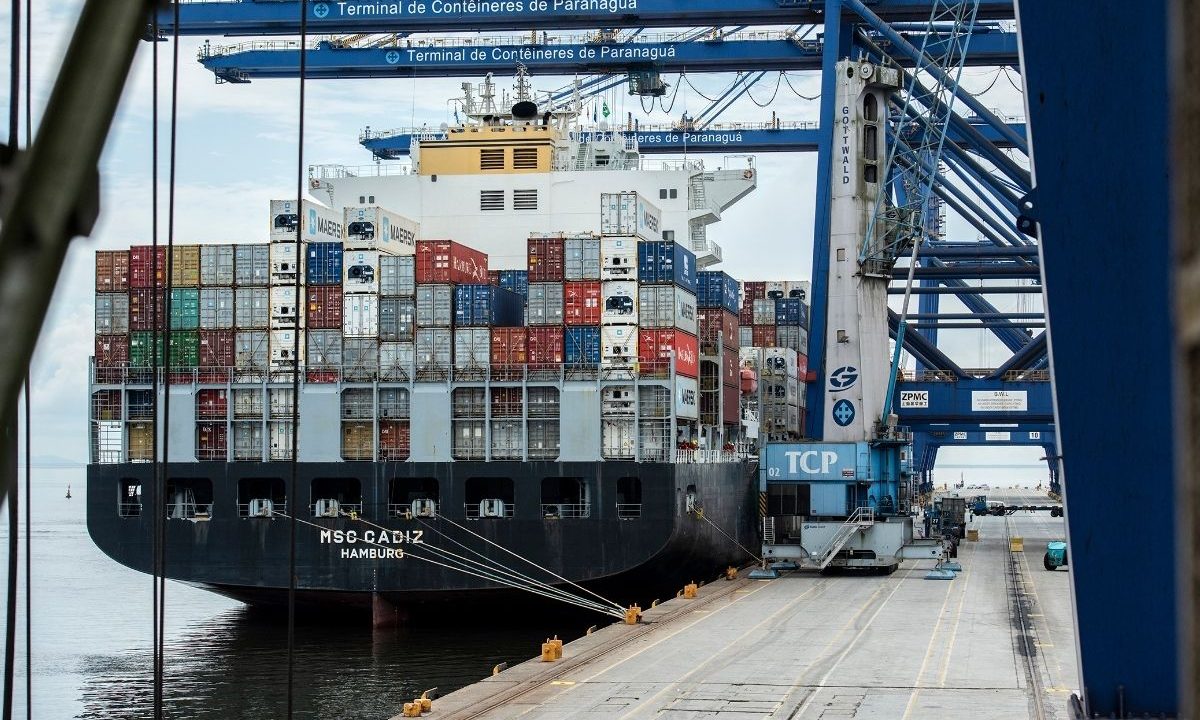 Navio porta-contêineres MSC Cadiz atracado no Terminal de Contêineres de Paranaguá (TCP) sob grandes guindastes azuis. A imagem mostra o carregamento de exportação em um porto brasileiro