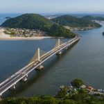 Ponte estaiada sobre o mar no litoral do Paraná ligando ilha à cidade com morros e praia ao fundo