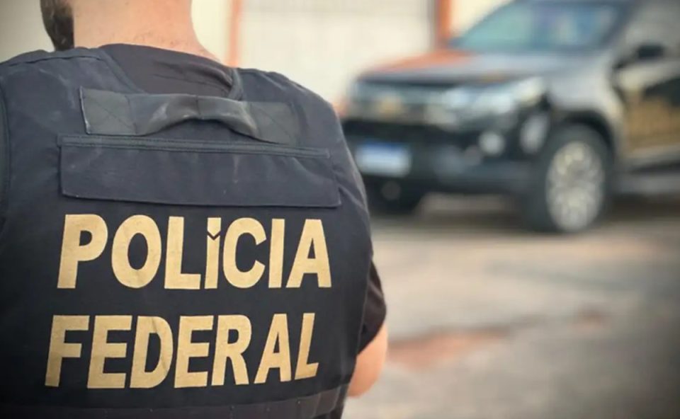 Foto mostra policial de costas para câmera, com o escrito "Polícia Federal" no colete à prova de balas, em alusão à operação que mira grupo envolvido com tráfico de drogas interestadual