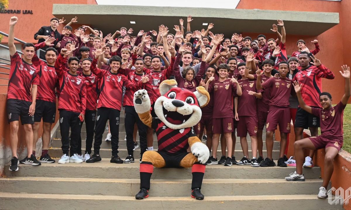 Foto em grupo com dezenas de jogadores das categorias de formação (Sub-15, Sub-17 e Sub-20) posicionados em uma escadaria externa de cor laranja. No centro, à frente de todos, o mascote Fura-Cão está sentado fazendo pose. Todos estão uniformizados.