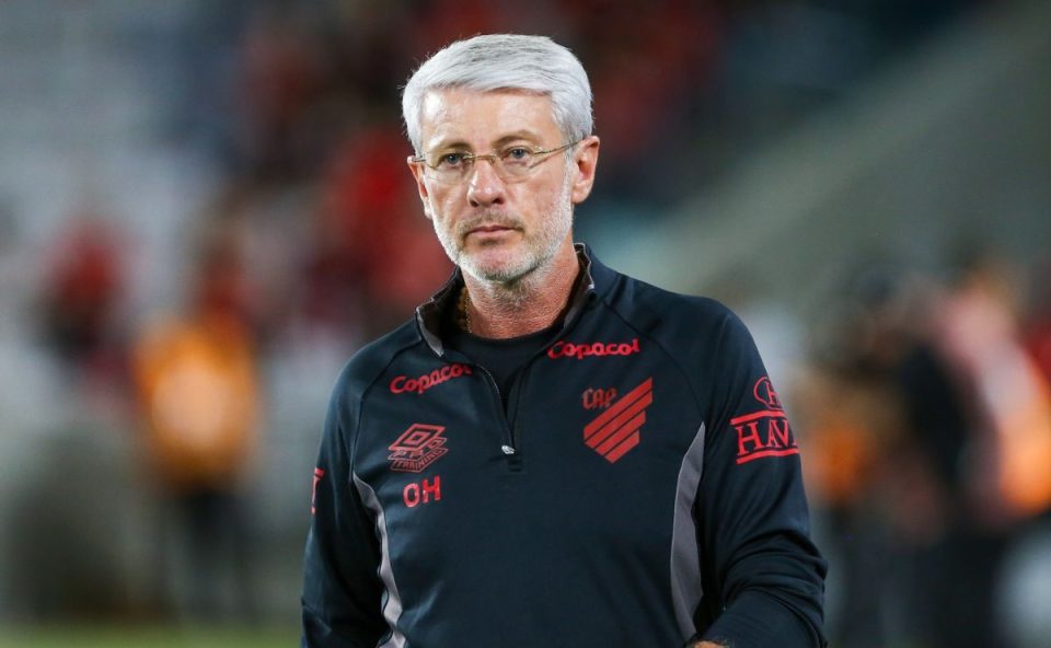 Odair Hellmann, técnico do Athletico, em pé à beira do campo durante partida, usando uniforme preto do clube, com expressão séria enquanto observa o jogo
