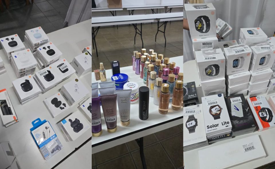 Mesas com produtos à venda em bazar beneficente, incluindo caixas de celulares, fones de ouvido e perfumes organizados lado a lado.