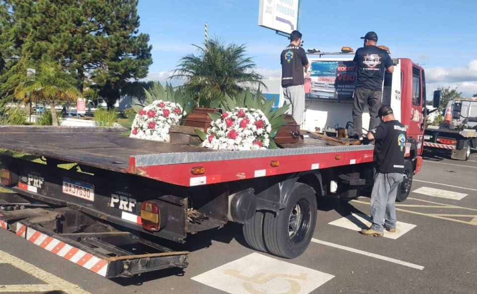 Caixão é transportado sobre caminhão guincho durante cortejo fúnebre em Curitiba