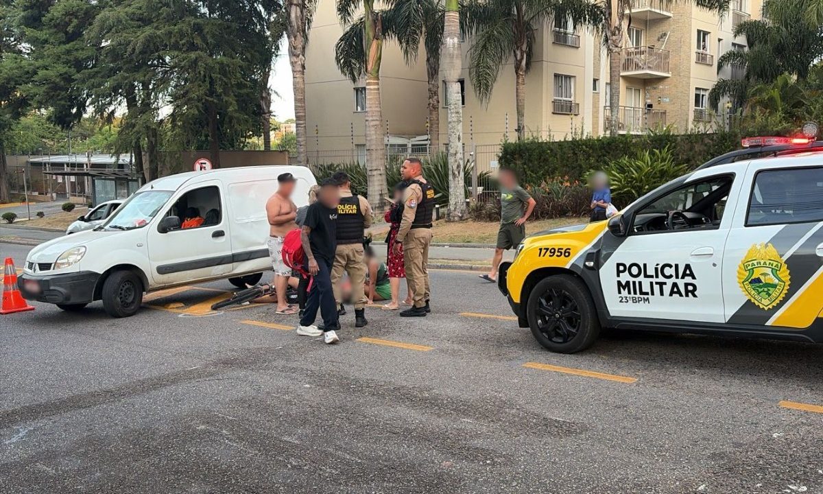 Viatura da Polícia Militar, policiais militares e pedestres durante atendimento de ciclista ferido após acidente com carro no bairro Campo Comprido, em Curitiba.