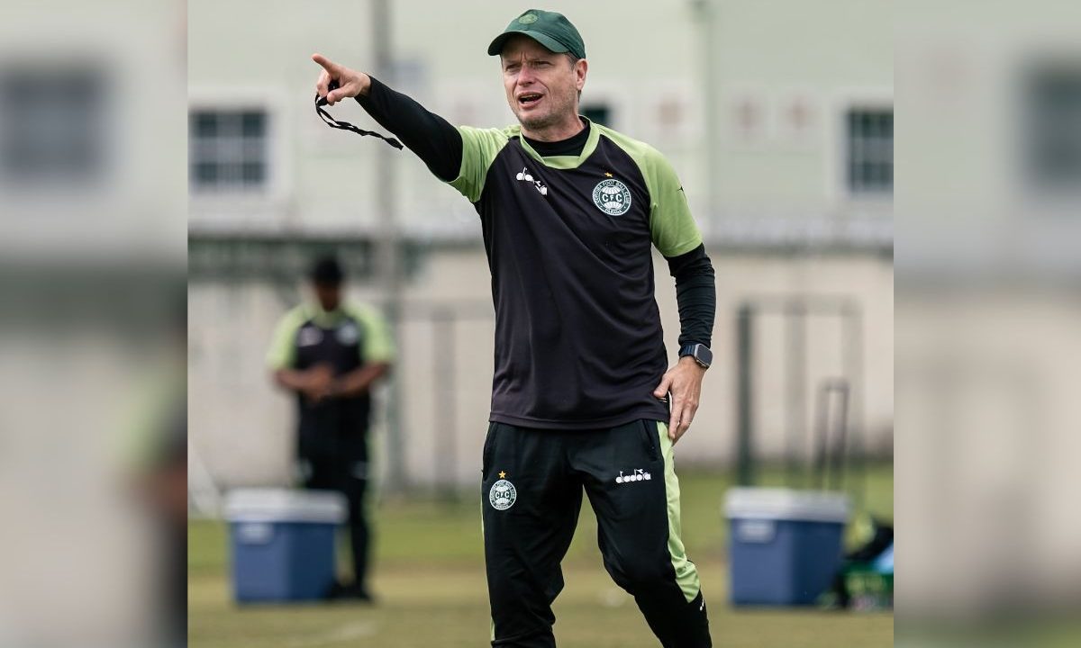 Fernando Seabra, treinador do Coritiba, acompanha treinamento da equipe em campo, vestindo uniforme esportivo e observando atentamente a atividade dos jogadores durante a preparação para partida do Campeonato Brasileiro.