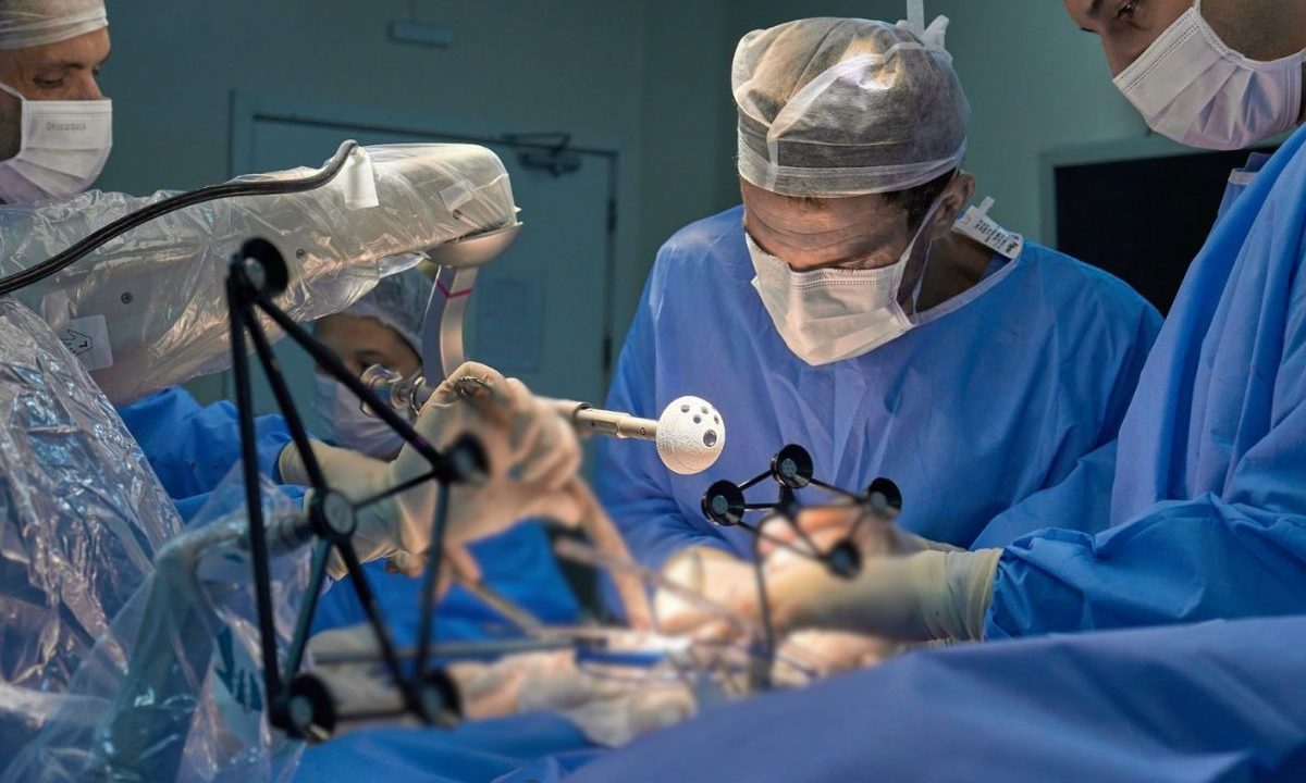 Equipe médica realiza cirurgia de prótese de quadril em sala hospitalar com uso de equipamentos modernos.