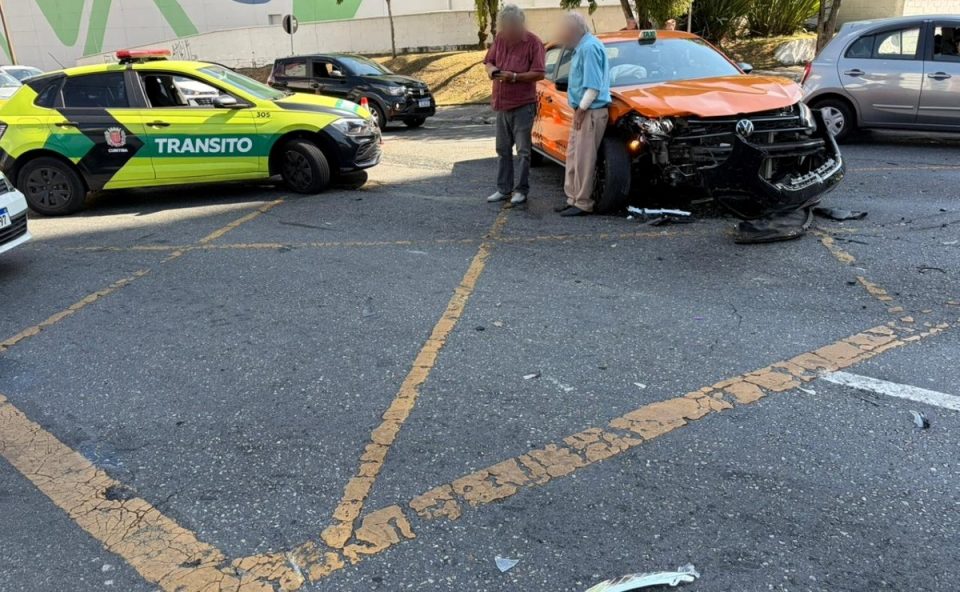 Taxista e outro homem parados ao lado de táxi envolvido em batida com três carros. Táxi laranja teve parte da frente destruída após colisão no Cabral. Família que estava em outro carro voltava de chá revelação
