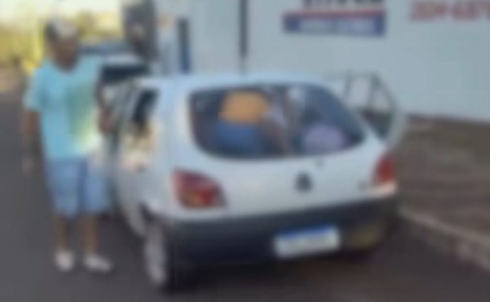Imagem mostra o motorista do Ford Fiesta com 11 pessoas descendo do veículo branco. O carro está estacionado. O carro é branco. Motorista está com uma camiseta verde clara e uma bermuda jeans, além de boné e tênis.
