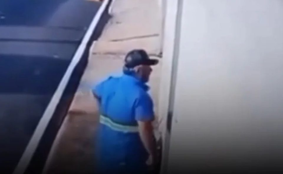 Foto mostra Sinério Omar da Costa Júnior, funcionário suspeito de matar o próprio chefe a tiros após uma advertência, parado em frente à casa da vítima. Ele usa um uniforme azul da empresa de saneamento Serviço Autônomo de Água e Esgoto (Saae) e um boné escuro.
