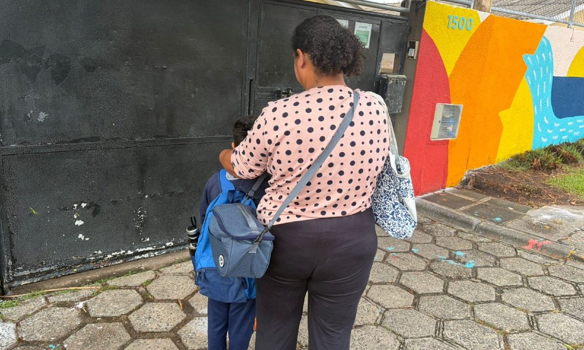 Foto mostra mãe ao lado do filho pequeno em frente a uma escola municipal do Bom Retiro que foi afetada pela greve de professores em Curitiba