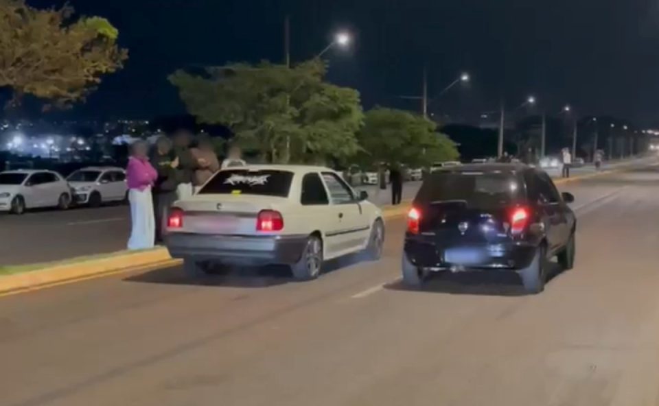 Foto mostra dois carros durante racha promovido por grupo alvo de operação. Testemunhas acompanham e assistem às arrancadas em avenida