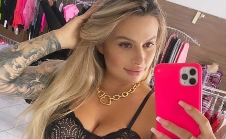 Trafigata, em prisão domiciliar, conta sobre própria história. Ela é loira, está com a mão no cabelo e com top preto. A foto foi tirada na frente do espelho. Ela segura o celular com capinha rosa.