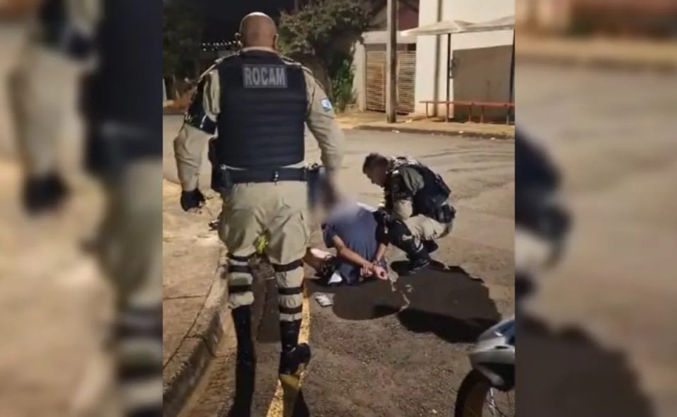 Foto tirada à noite mostra suspeito de matar homem a tesouradas sendo algemado por policiais militares no chão