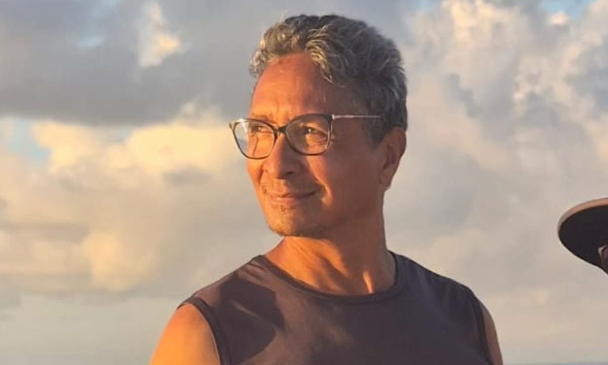 Image mostra Roberto de Godoi, idoso com epilepsia que está desaparecido desde uma viagem para o litoral do Paraná. Ele tem cabelo grisalho, usa óculos de grau e regata. Ele é iluminado pelo sol.