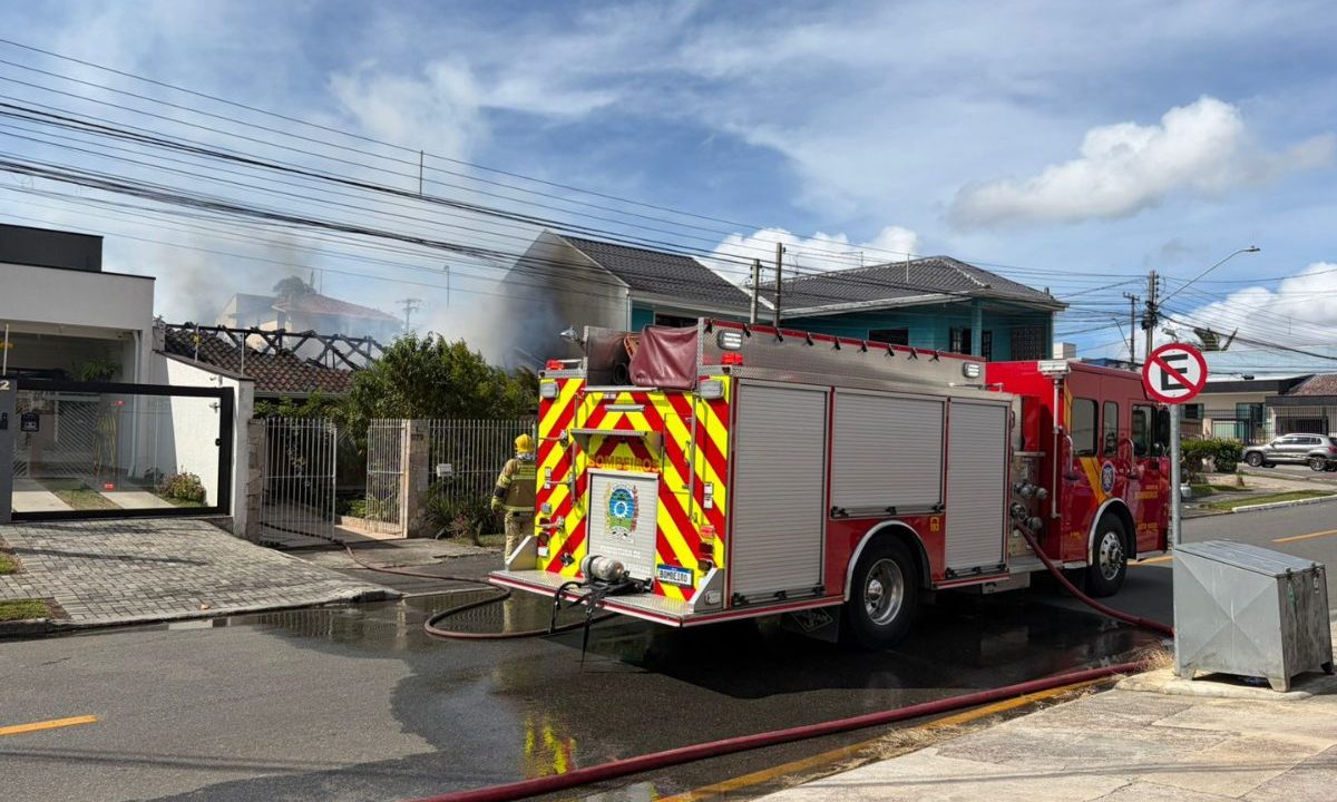 Imagem mostra o incêndio em São José dos Pinhais. Um caminhão do Corpo de Bombeiros aparece na frente. Atrás, o imóvel pegando fogo.