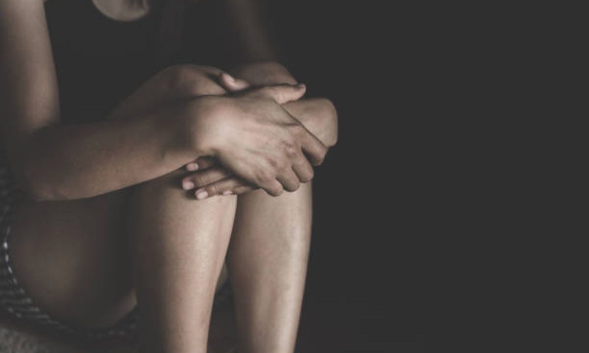 Mulher abraçando os próprios joelhos no escuro