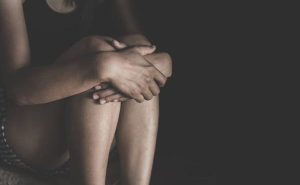 Mulher abraçando os próprios joelhos no escuro