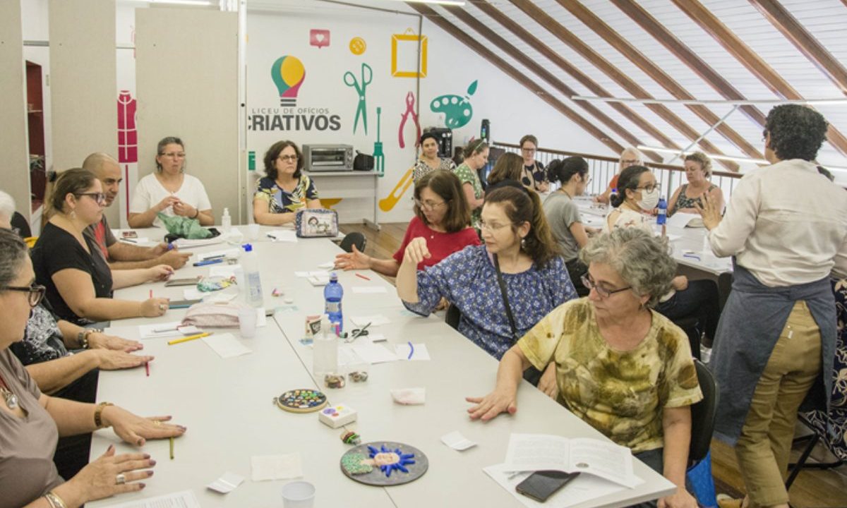 Grupo de pessoas participa de oficina de artesanato em sala do Liceu de Ofícios Criativos, trabalhando em mesas com materiais manuais.