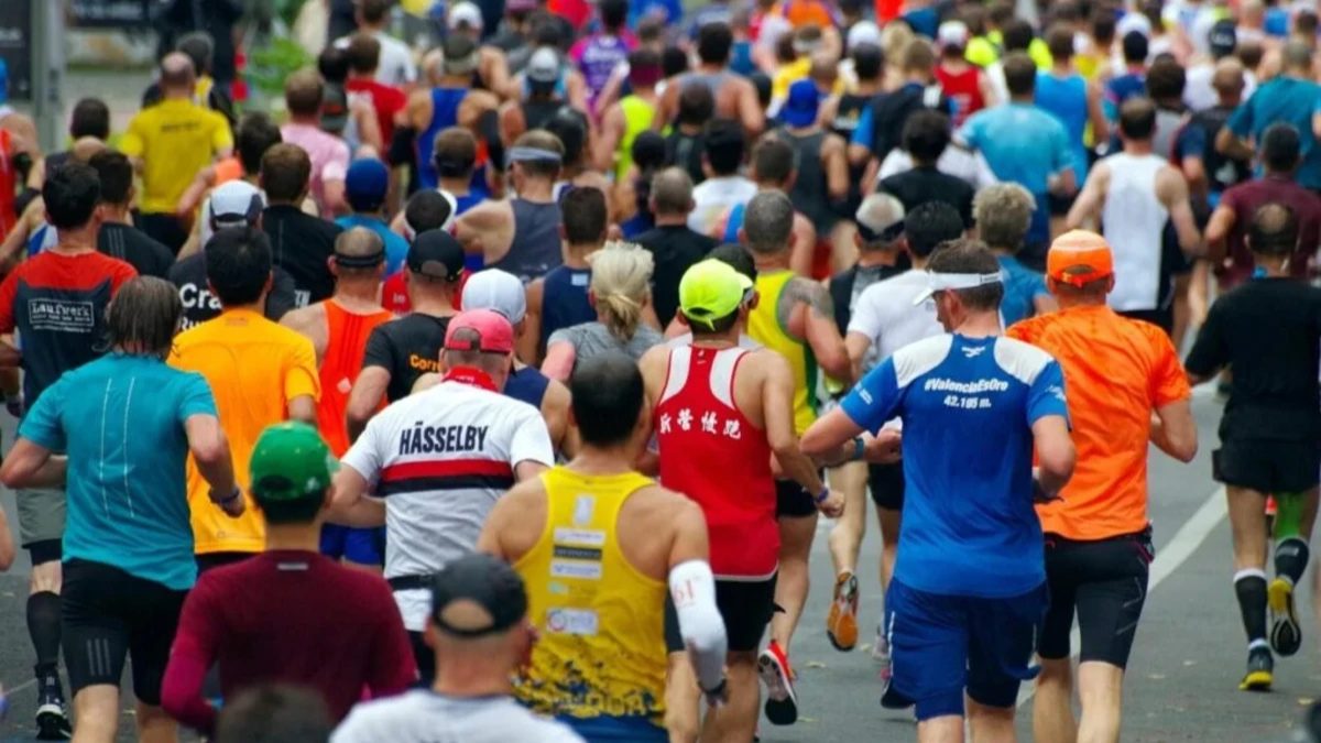 Foto de uma multidão de corredores, vistos de costas, correndo juntos em uma rua durante a Maratona Internacional do Paraná. Eles vestem roupas esportivas coloridas e a imagem captura a energia da largada da prova.