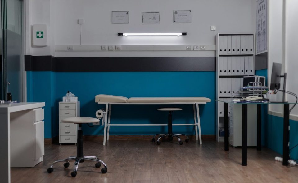 Consultório médico vazio com maca, equipamentos e mesa de atendimento