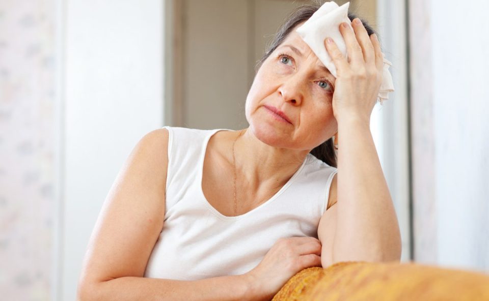 Mulher com expressão de cansaço enxugando o suor da testa, representando sintomas de calorão na menopausa